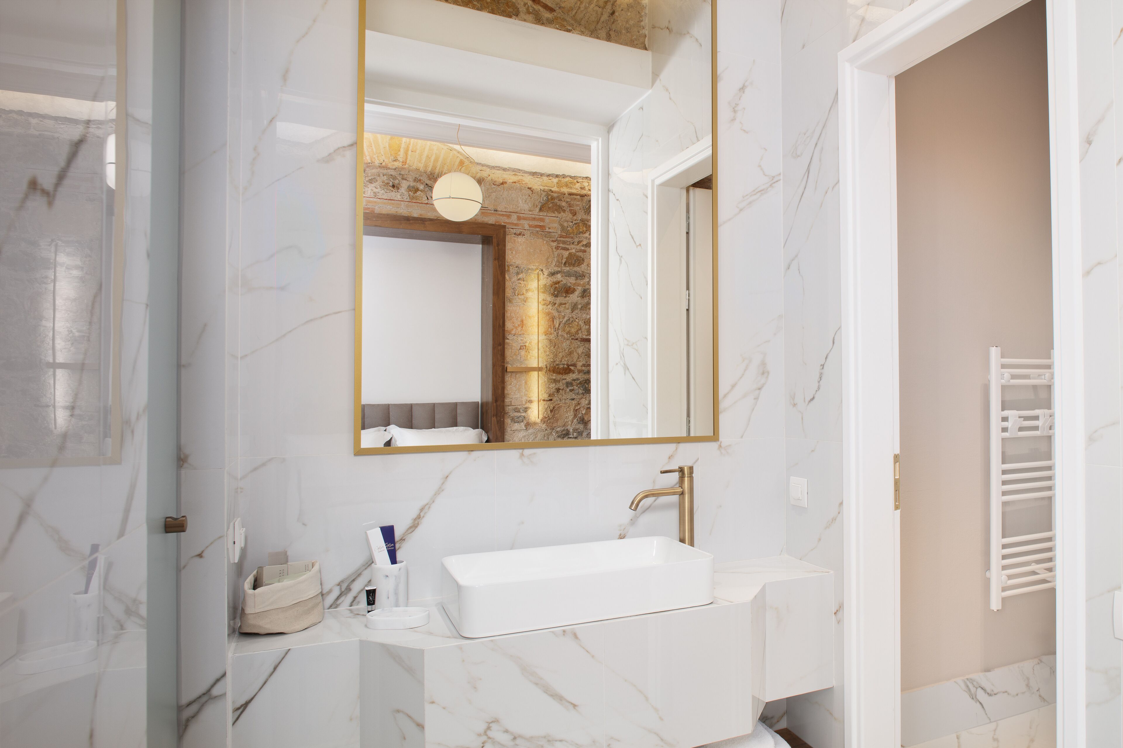 A modern bathroom with a white marble sink, a large mirror, and a stone accent wall.