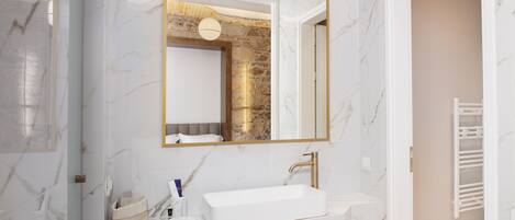 A modern bathroom with a white marble sink, a large mirror, and a stone accent wall.