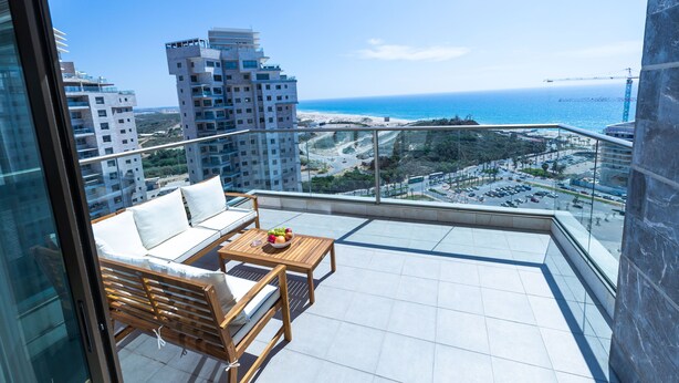 Un balcone con un divano, un tavolo in legno con frutta e vista sull'oceano e sulla città.