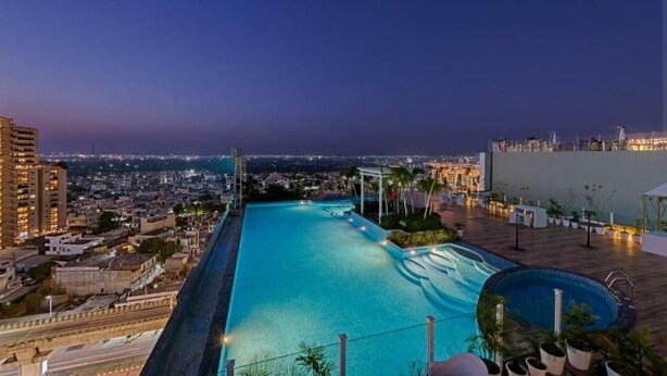 Una piscina en la azotea con vistas a la ciudad, rodeada de edificios y un cielo despejado.