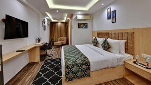 Una habitación de hotel con cama, mesita de noche, televisión, escritorio, silla y una planta pequeña.