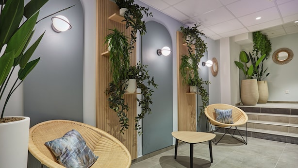A modern interior with wicker chairs, a wooden wall, and potted plants. - Appart'hôtel Odalys City - Nîmes Arènes - Palais des Congrès (Nîmes)