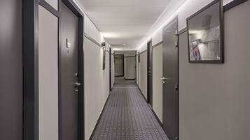 Un couloir d’hôtel avec des portes des deux côtés, une moquette à motifs et un tableau encadré sur le mur de droite.