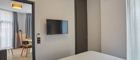 A modern hotel room with a large bed, a flat-screen TV mounted on the wall, a door, and a window with curtains.