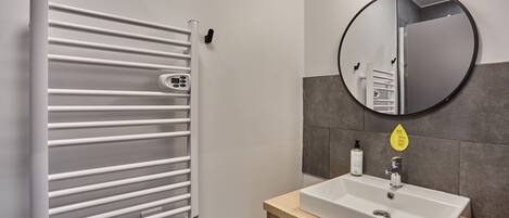 A modern bathroom with a white towel warmer, a round mirror, and a white sink.