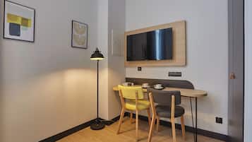A small room with a desk, two chairs, a television, and artwork on the walls.