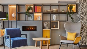 A modern living room with a fireplace, two chairs, a round table, and a bookshelf with decorative items. - Appart'hôtel Odalys City - Nîmes Arènes - Palais des Congrès (Nîmes)