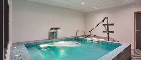 A modern indoor swimming pool with clear water, a changing room, and a door to the right.