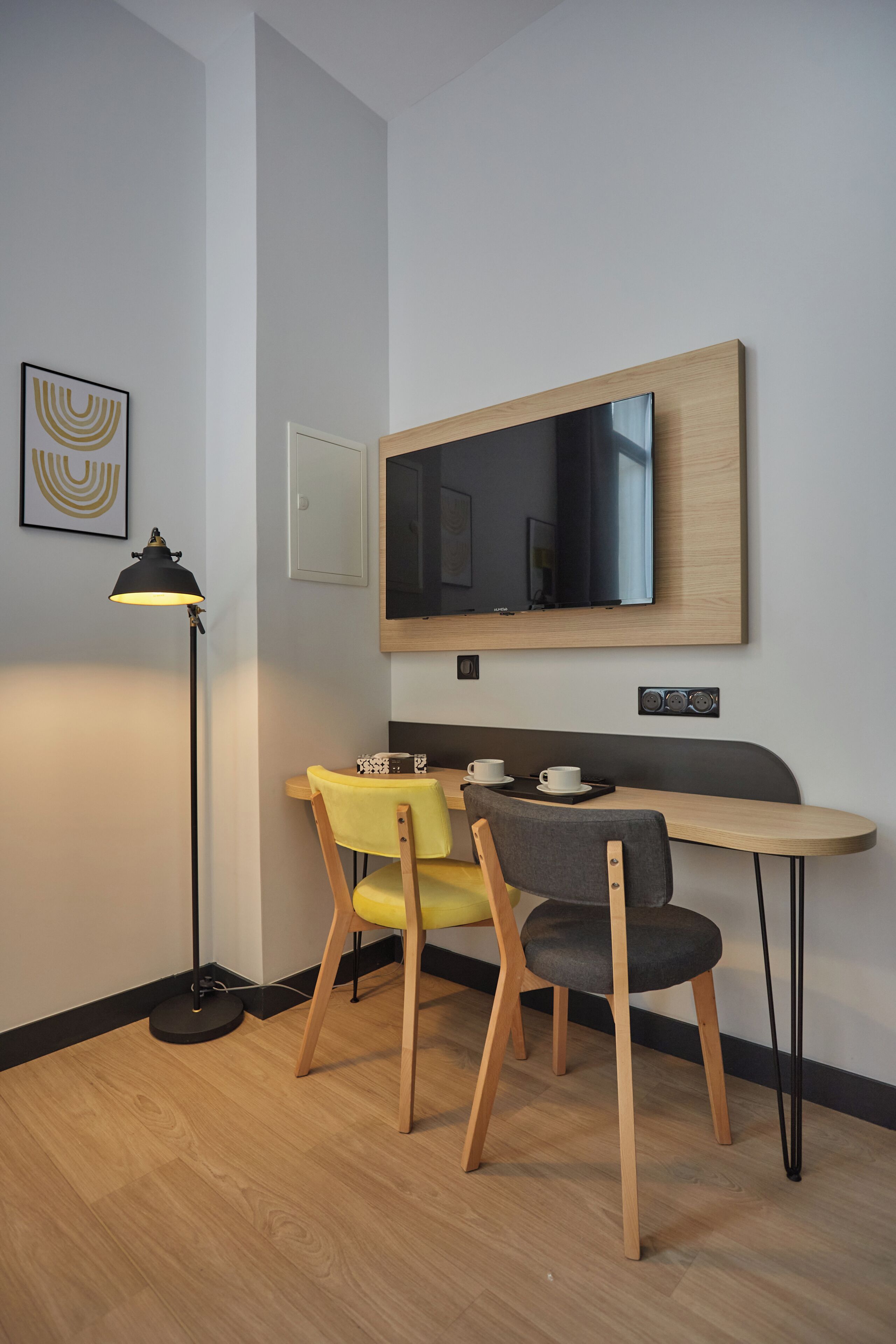 Una habitación moderna con escritorio, dos sillas, una lámpara de pie y un espejo grande en la pared.