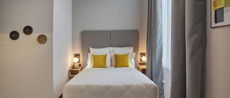 Un dormitorio moderno con cama, lámparas de noche, un banco y decoración en la pared.