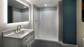 Un baño moderno con tocador, un espejo grande, ducha e inodoro.