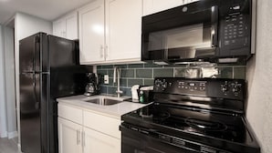 Una cocina moderna con armarios blancos, un refrigerador negro, un microondas negro y una estufa negra.
