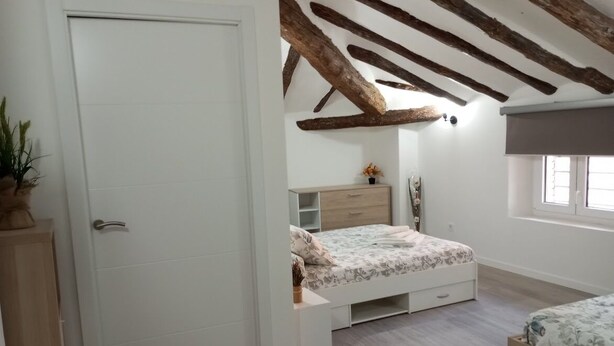 A bedroom with a wooden ceiling, a bed, a bedside table, and a window. - Apartamento Ático, ideal familias y amigos cerca de Senda Viva y Bardena Real. (Arguedas)