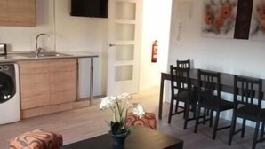 A modern living room with a sofa, a coffee table with a vase of flowers, a dining area with a table and chairs, a kitchen with a sink and cabinets, and a television mounted on the wall. - Apartamento Ático, ideal familias y amigos cerca de Senda Viva y Bardena Real. (Arguedas)