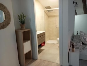A bedroom with a bed, a bedside table, a mirror, and a small plant.