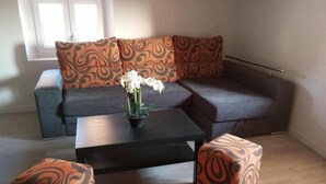 A living room with a dark grey sofa, patterned cushions, a black coffee table, and two matching ottomans. There is a potted plant with white flowers on the coffee table. - Apartamento Ático, ideal familias y amigos cerca de Senda Viva y Bardena Real. (Arguedas)