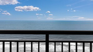 Blick auf das Meer vom Balkon mit Geländer, klarer Himmel und vereinzelten Wolken.