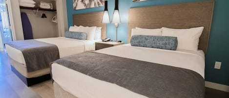 A hotel room with two beds, a nightstand with a lamp, and a wall with palm leaf artwork.