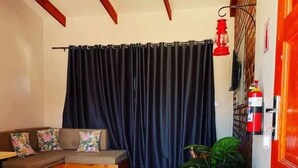 Een woonkamer met een bank, een bijzettafeltje, een koelkast en een gordijn.