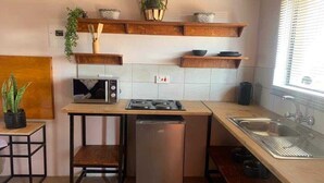 Een compacte keuken met een magnetron, fornuis en wastafel, houten planken erboven en een kleine koelkast.