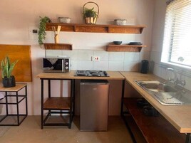 Una cocina compacta con microondas, estufa y lavamanos, repisas de madera arriba y un refrigerador pequeño.