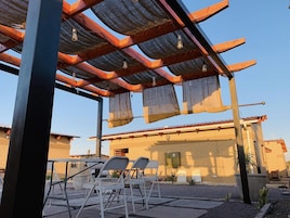 Un área de estar al aire libre con sillas metálicas y una estructura de pérgola.