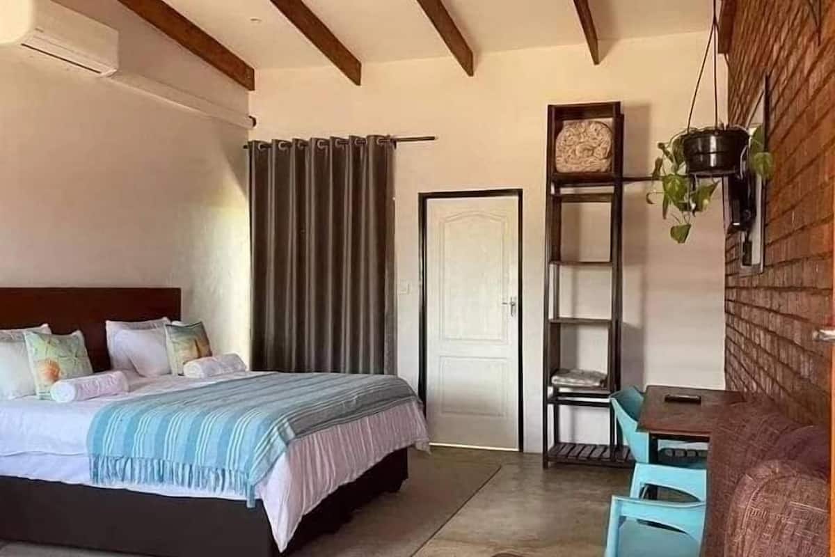 Un dormitorio con una cama, un escritorio, una silla, una estantería con plantas y una puerta.