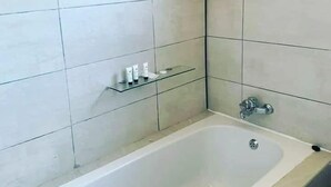 Een badkamer met een badkuip, betegelde muren en een plank met toiletartikelen.