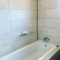 Un baño con bañera, paredes de azulejos y un estante con artículos de aseo.