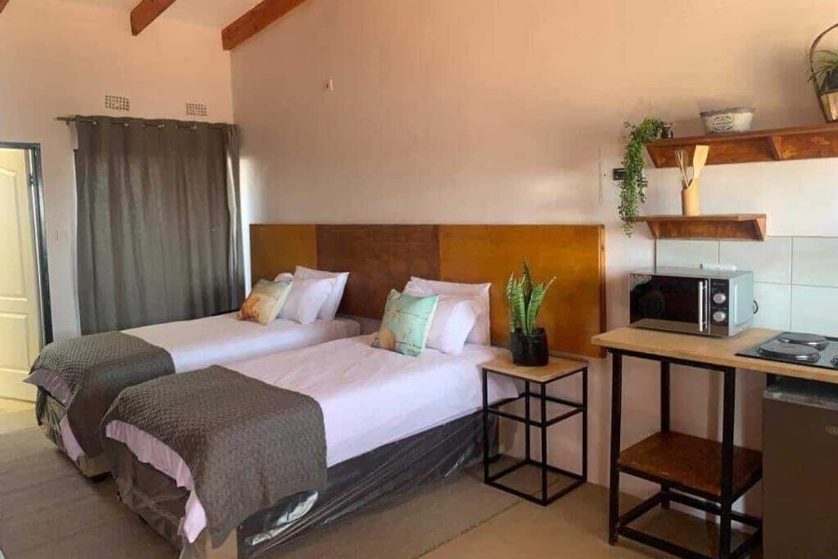 Un dormitorio con dos camas, techo de madera, una mesita con microondas y una planta.
