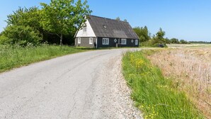 A rural road leading to a traditional house with a sloped roof and white trim.