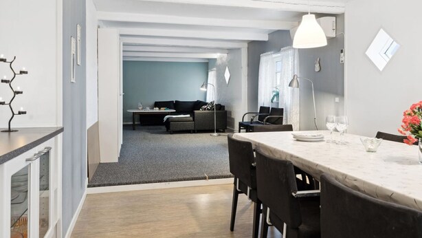 A modern kitchen with a dining area, a living room in the background, and a view of the cityscape.