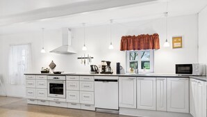 A modern kitchen with white cabinetry, a central island with appliances, pendant lights, and a window with a view.