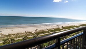 Vista sulla spiaggia da un balcone con ringhiera, spiaggia sabbiosa e oceano.