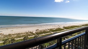 A beach view from a balcony with a railing, sandy beach, and ocean.