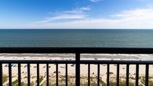 A beach view from a balcony with a railing, sandy beach, and ocean.