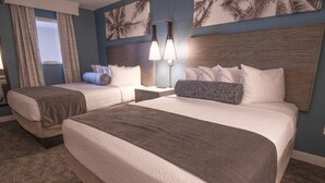 A hotel room with two beds, a nightstand, a lamp, and palm tree artwork on the wall.