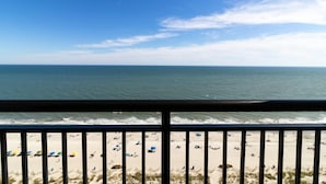 Vista a la playa desde un balcón con barandilla, playa de arena y océano.