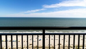 Blick auf einen Strand vom Balkon aus, mit Geländer, Sand und Meer.