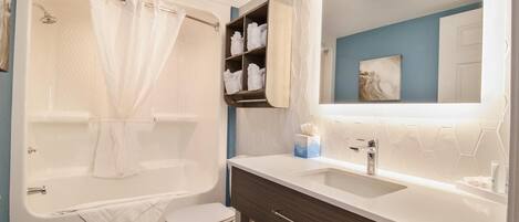 Un baño moderno con bañera, inodoro, tocador y un espejo grande.