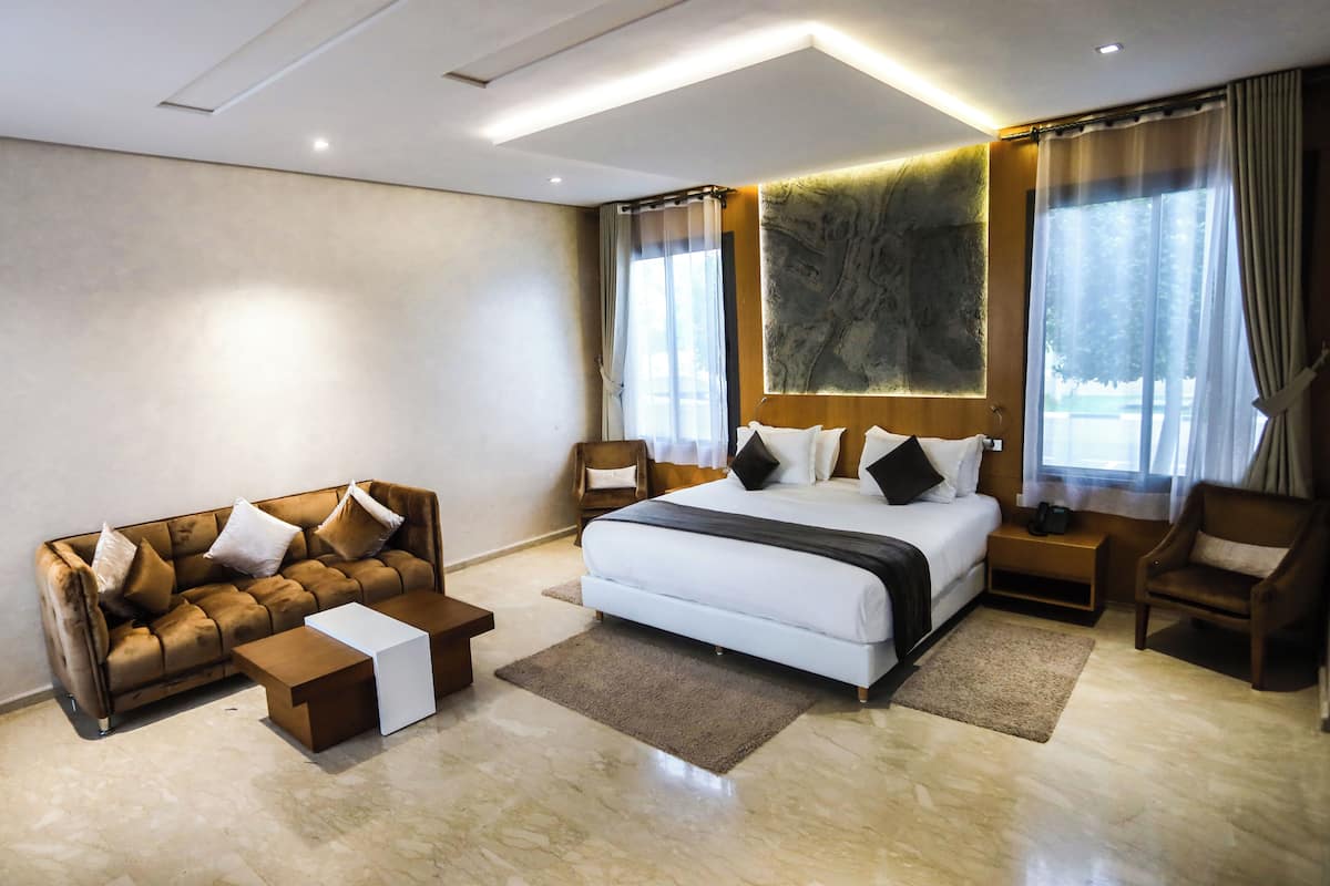 A modern bedroom with a large bed, a brown leather sofa, a small coffee table, and a wooden nightstand.