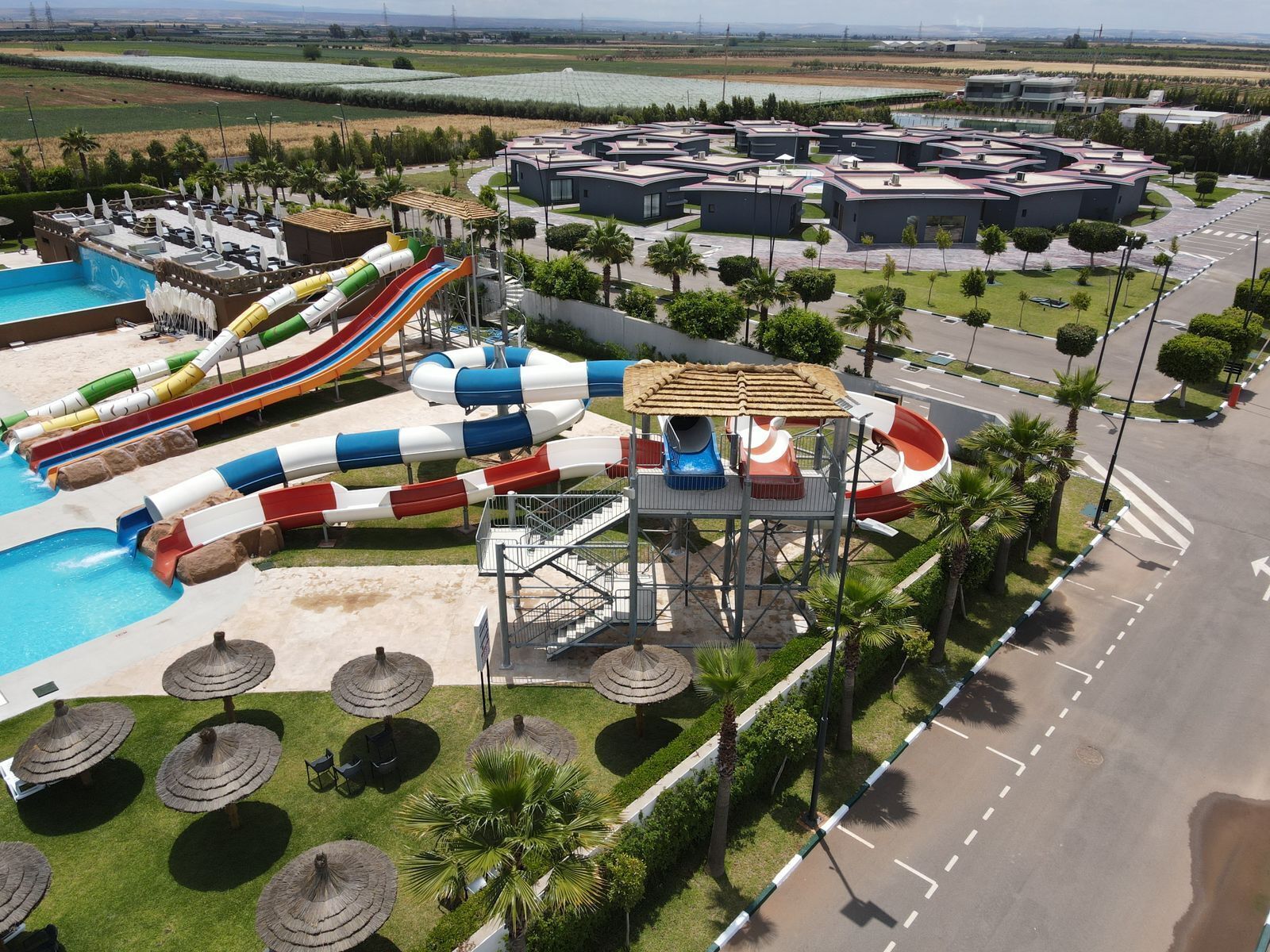 A water park with multiple slides and a pool, surrounded by palm trees and a parking area.