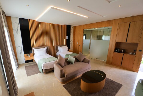 A modern hotel room with two beds, a sofa, a coffee table, and a wooden cabinet.
