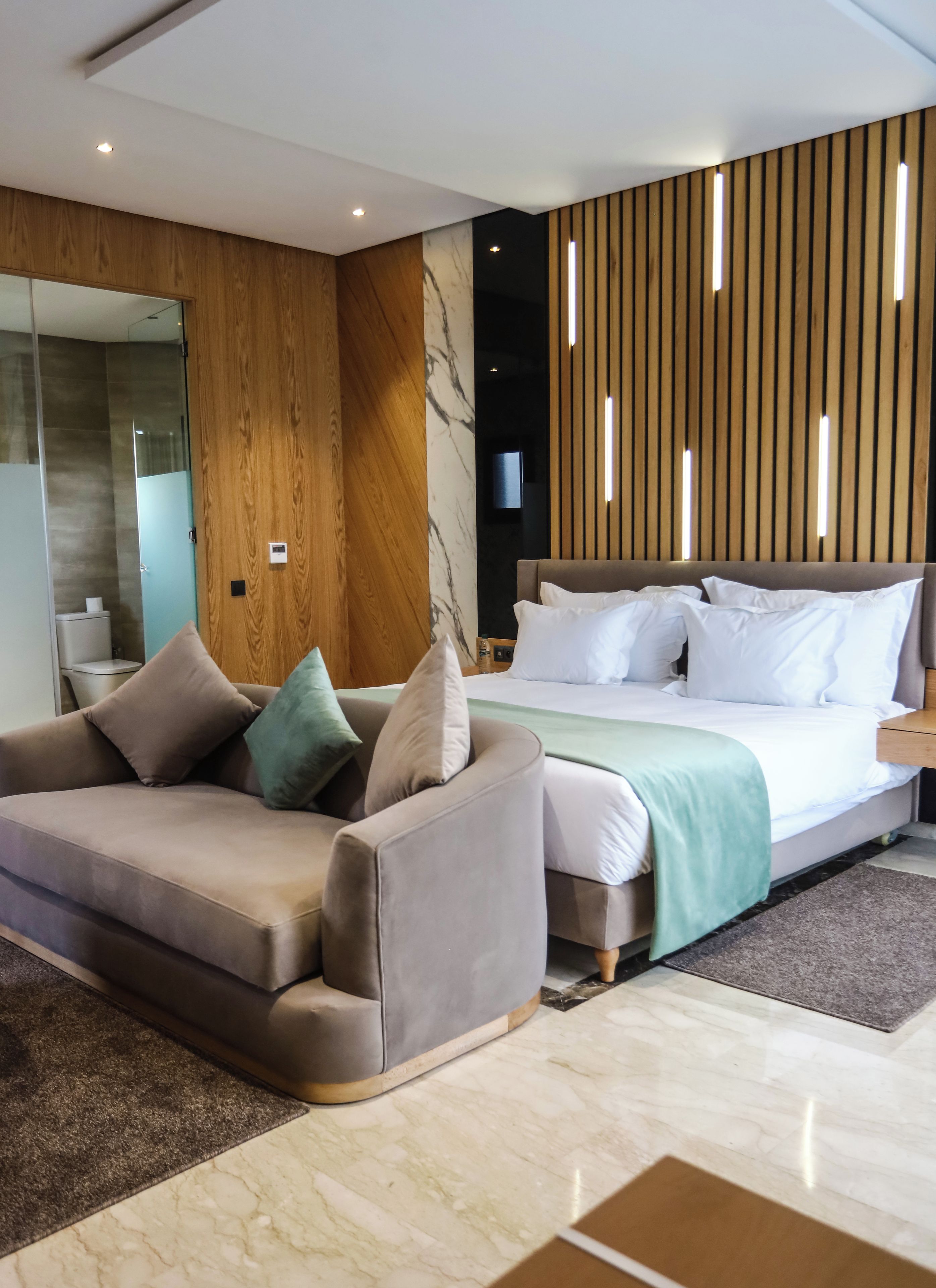 A modern bedroom with a bed, a sofa, a wooden panel wall, and a television.