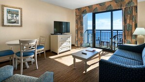 A hotel room with a balcony, a television, a dining area with chairs, a sofa, and a table. - Unmatched Oceanfront Serenity on the 10th Floor (Myrtle Beach)