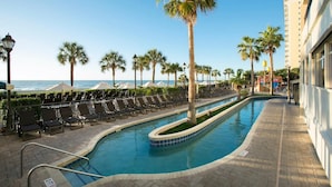 A pool area with lounge chairs, palm trees, and a view of the ocean.