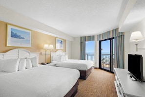 Habitación de hotel con dos camas, televisor, escritorio y balcón con vistas.