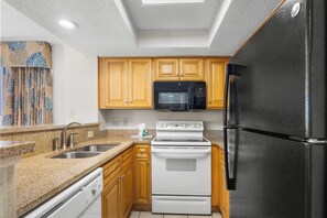 Una cocina con gabinetes de madera, un refrigerador negro, un microondas, una estufa y un lavamanos.