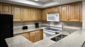 A kitchen with wooden cabinets, a black refrigerator, a white microwave, a stove, and a granite countertop. - Your Oceanfront Oasis 9th Floor 3 Bedroom Deluxe (Myrtle Beach)