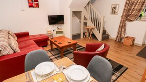 A furnished living room with a red sofa, a wooden dining table set for four, and a staircase leading to an upper level.